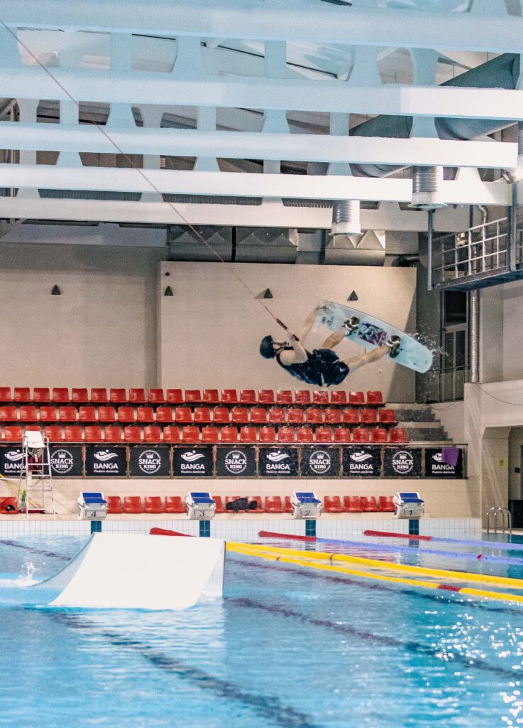 Vandenlentininkas atlieka tiuką su vandenlentę vandenlenčių parke po stogu